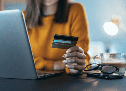 A woman holds a credit card next to her laptop