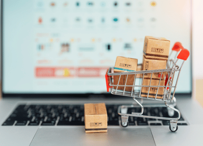 A tiny toy shopping cart filled with tiny packages on a laptop