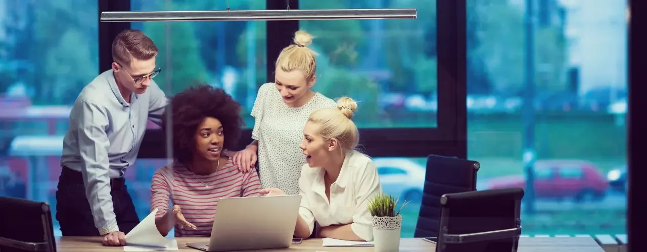A group of colleagues sit at a computer and talk