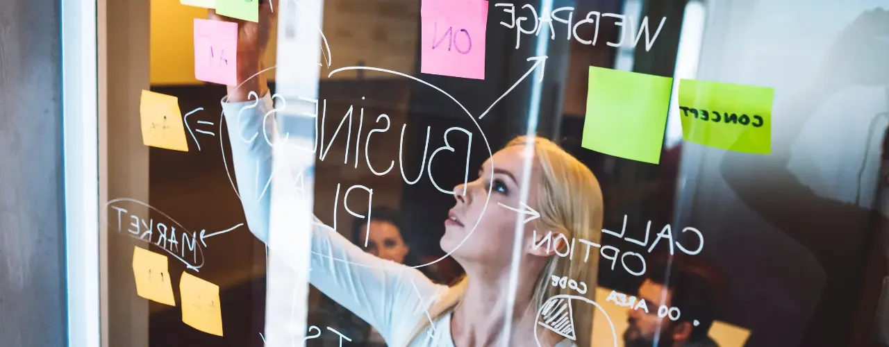 A woman is working on a whiteboard with sticky notes while her colleagues are watching.